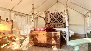 Interior de una tienda de campaña con una cama con dosel, un cofre de madera y un banco.