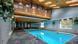 An indoor swimming pool with a wooden balcony, tiled walls, and hanging flower baskets.