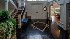 A grand entrance with a black tiled floor, a wooden staircase, a blue bench, and a white door with a gold handle.