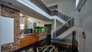 A spacious foyer with a polished black floor, a stone accent wall, a staircase with ornate black railings, and a seating area with a blue bench.