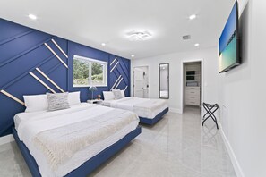 Un dormitorio moderno con dos camas, un ventanal grande, un televisor y un vestidor.