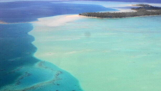 Vue aérienne d’une zone côtière avec des eaux d’un bleu limpide, des plages de sable et une petite île couverte d’une végétation luxuriante.