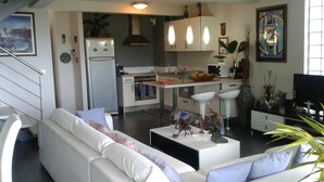 Une cuisine moderne avec des meubles blancs, un réfrigérateur et un coin repas comprenant une table et des chaises blanches.