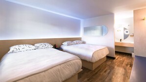 Une chambre d’hôtel moderne avec deux lits simples, un plancher en bois, un grand miroir et une petite salle de bain.