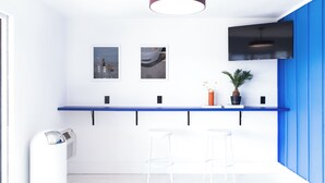 Une cuisine moderne avec un plan de travail bleu, deux tabourets de bar, un téléviseur fixé au plafond et une plante en pot.