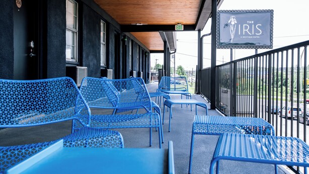 Façade d’un hôtel avec un espace extérieur abrité, comprenant des chaises et des tables en métal bleues, un panneau indiquant la sortie et une enseigne pour «
The Iris Boutique Hotel
».