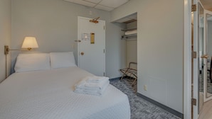 A hotel room with a large bed, a bedside lamp, a door with a plaque, a coat rack, and a mirror. - Converted Studio Apartment. - Great Location! (Nashville)