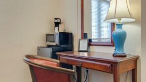 A hotel room with a wooden desk, a red upholstered chair, a blue lamp, a coffee maker, a microwave, and a framed certificate on the desk. - Converted Studio Apartment. - Great Location! (Nashville)