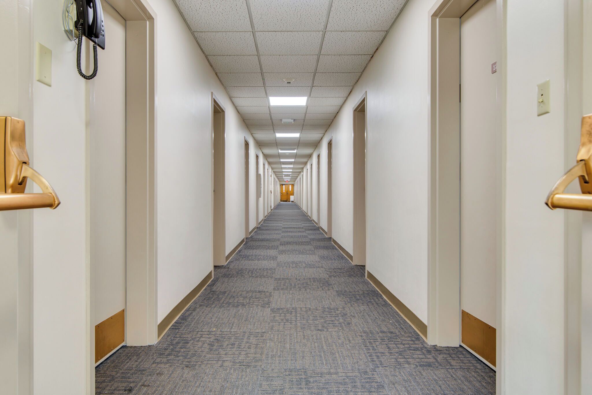 A long, narrow hotel corridor with carpeted floors and white walls.