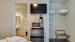 Habitación de hotel con cama, microondas, cafetera, televisor y armario con estantes.