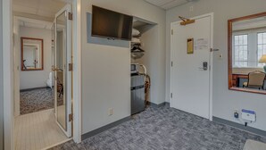 A hotel room with a kitchenette, a flat-screen TV mounted above the counter, a door with a mirror, and a window with blinds. - Cozy Suite in a Revamped Dorm Room! (Nashville)