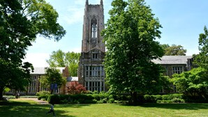A historic building with a prominent tower, surrounded by lush greenery and a well-maintained lawn.
