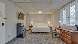 A hotel room with a bed, desk, chair, dresser, microwave, and a TV on the wall.