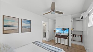 Ein Schlafzimmer mit einem Bett, einem Deckenventilator, einem Fernseher und zwei Bildern mit Strandmotiv an der Wand.
