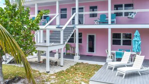 A two-story house with a pink exterior, a covered patio with white furniture, and a staircase leading to the upper floor. - Lillian's Downstairs - Island Comfort & Charm (Green Turtle Cay)