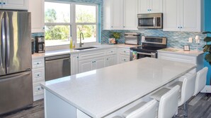A modern kitchen with white cabinets, stainless steel appliances, and a large island with bar stools. - Lillian's Downstairs - Island Comfort & Charm (Green Turtle Cay)