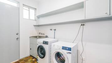 A laundry room with two washing machines, a sink, and a tiled floor.