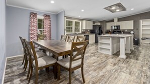 Una cocina moderna con armarios blancos, una isla central y un comedor con sillas y una mesa de madera.