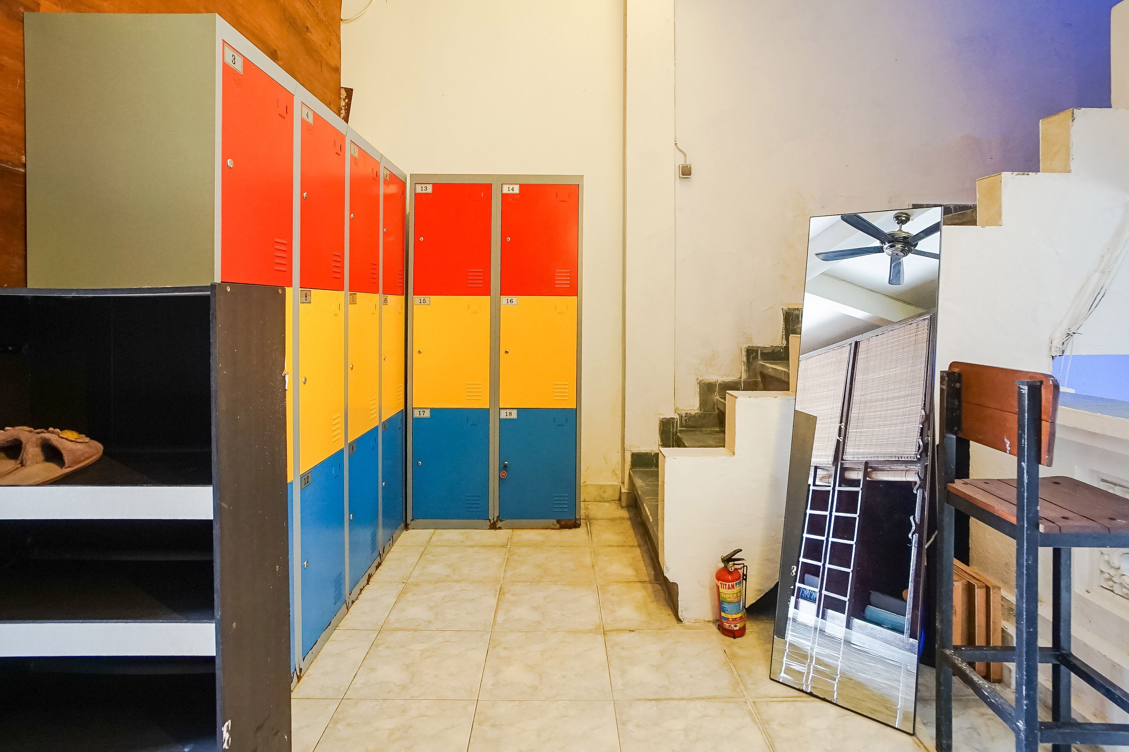 A locker room with multiple lockers in red, yellow, and blue, a fire extinguisher, and a ceiling fan.
