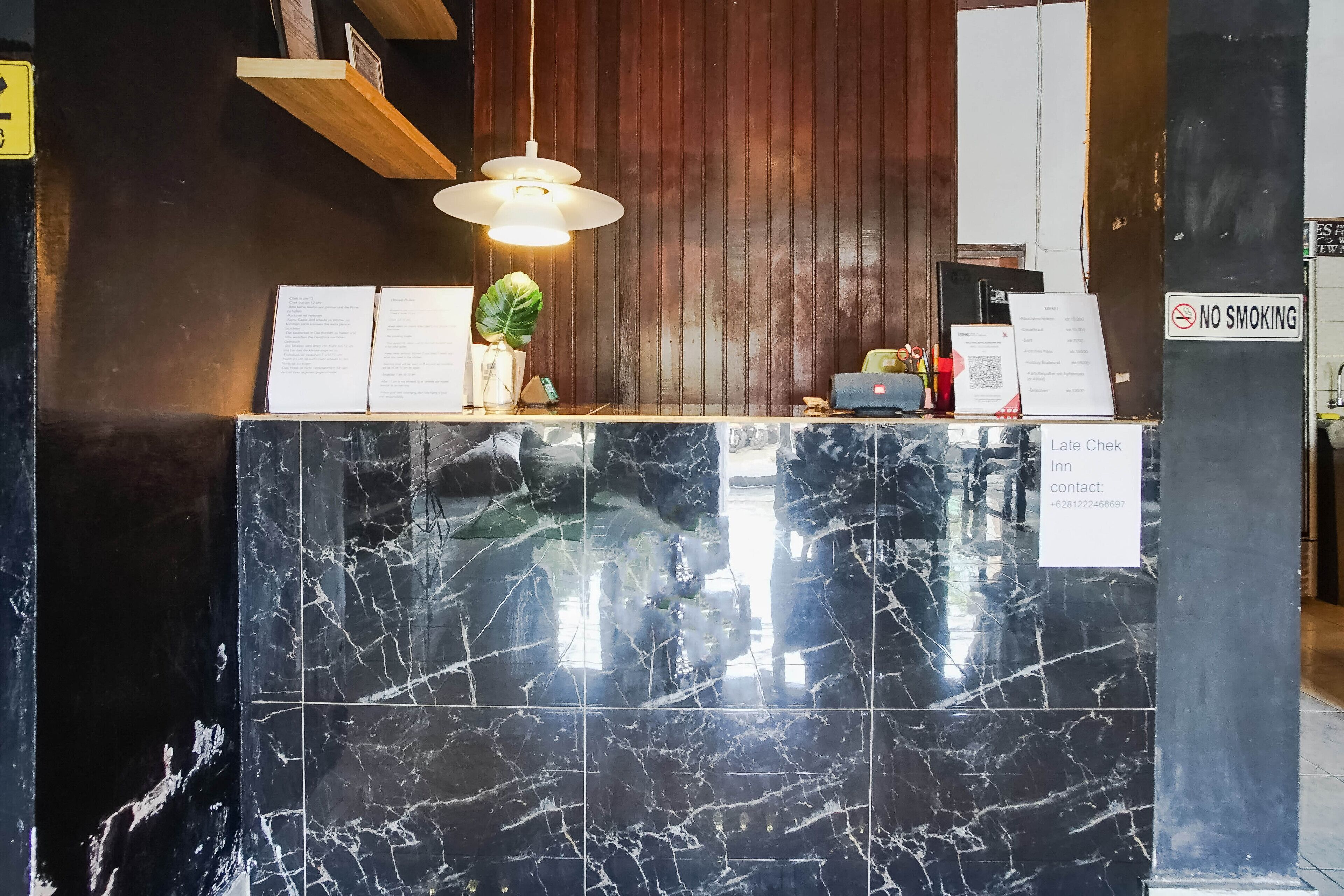 A reception desk with a marble counter, a hanging light fixture, a menu board, and a 'No Smoking' sign.