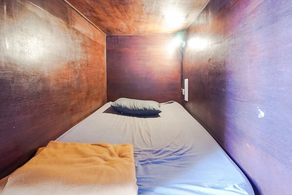 Una habitación pequeña y estrecha con una cama individual, una almohada y una manta.
