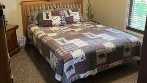 A bedroom with a wooden bed, a quilt with animal prints, a painting of a moose, and a window with blinds. - A peaceful getaway just minutes from Traverse City! The perfect Up North retreat (Traverse City)