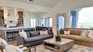 A spacious living area with a grey sofa, a beige sofa, and a wooden coffee table. There are two chairs and a dining table with chairs in the background.