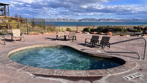 A hot tub with lounge chairs, a warning sign, and a view of mountains and a body of water.