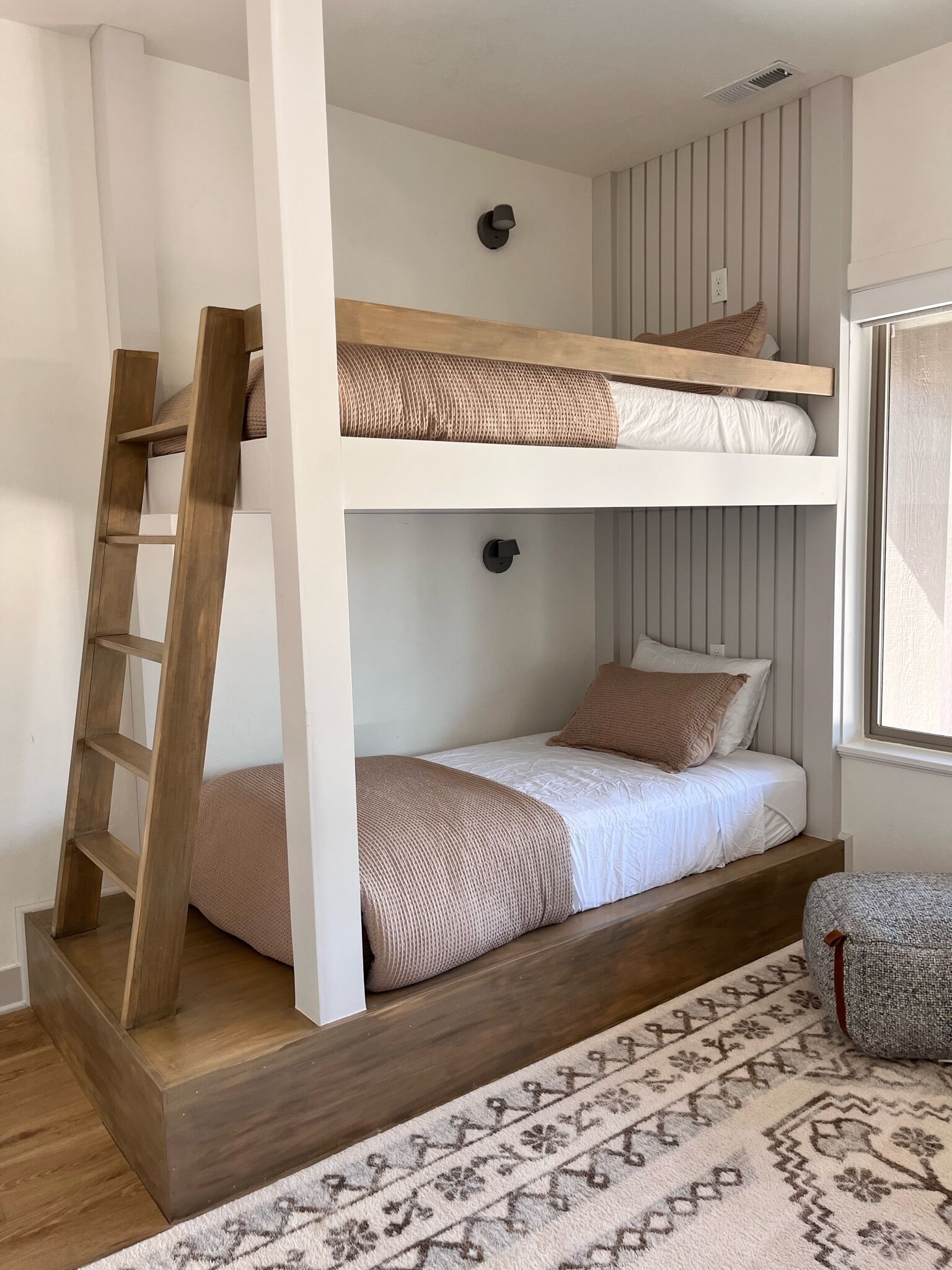 Un lit superposé avec une échelle en bois, des murs blancs et un tapis à motifs.