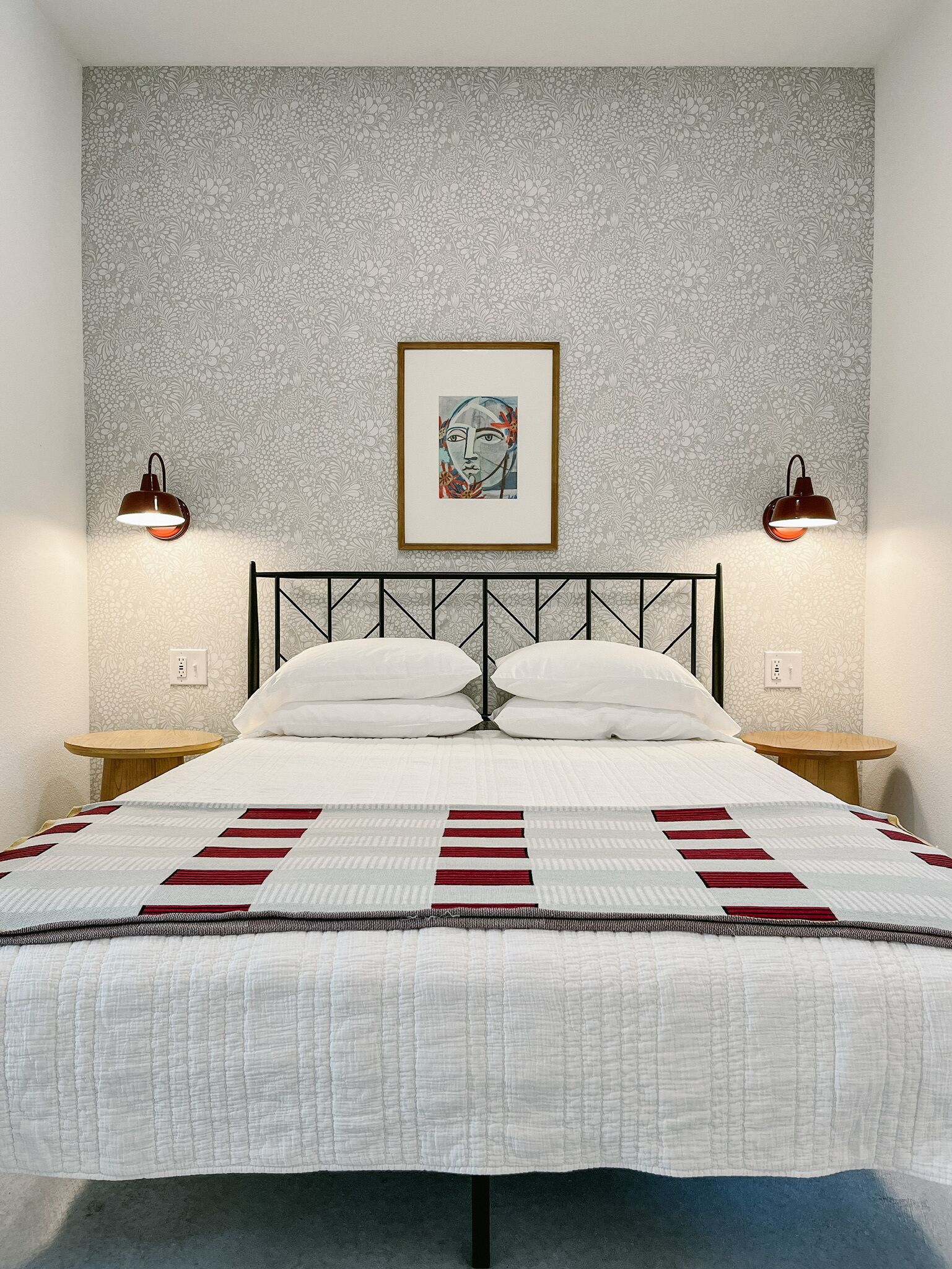 A bedroom with a bed, two bedside tables, a framed artwork above the bed, and a patterned wall.