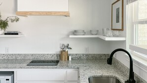 A modern kitchen with white cabinetry, granite countertops, a stainless steel sink, and black pendant lights. - Elegant studio near downtown (Abilene)