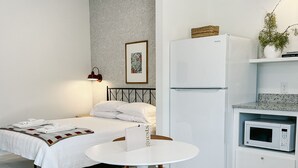 A compact hotel room with a bed, a small round table with a chair, a kitchenette with a microwave, and a refrigerator. - Elegant studio near downtown (Abilene)