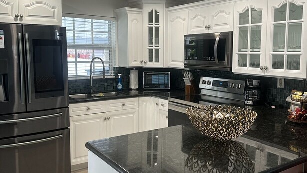 A modern kitchen with white cabinetry, stainless steel appliances, and a black granite countertop. - Do you want to select a perfect place to know Miami?. This is R and R Hostal.  (Miami)