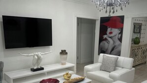 A modern living room with a flat-screen TV, white sofas, a coffee table, and a chandelier. - Do you want to select a perfect place to know Miami?. This is R and R Hostal.  (Miami)