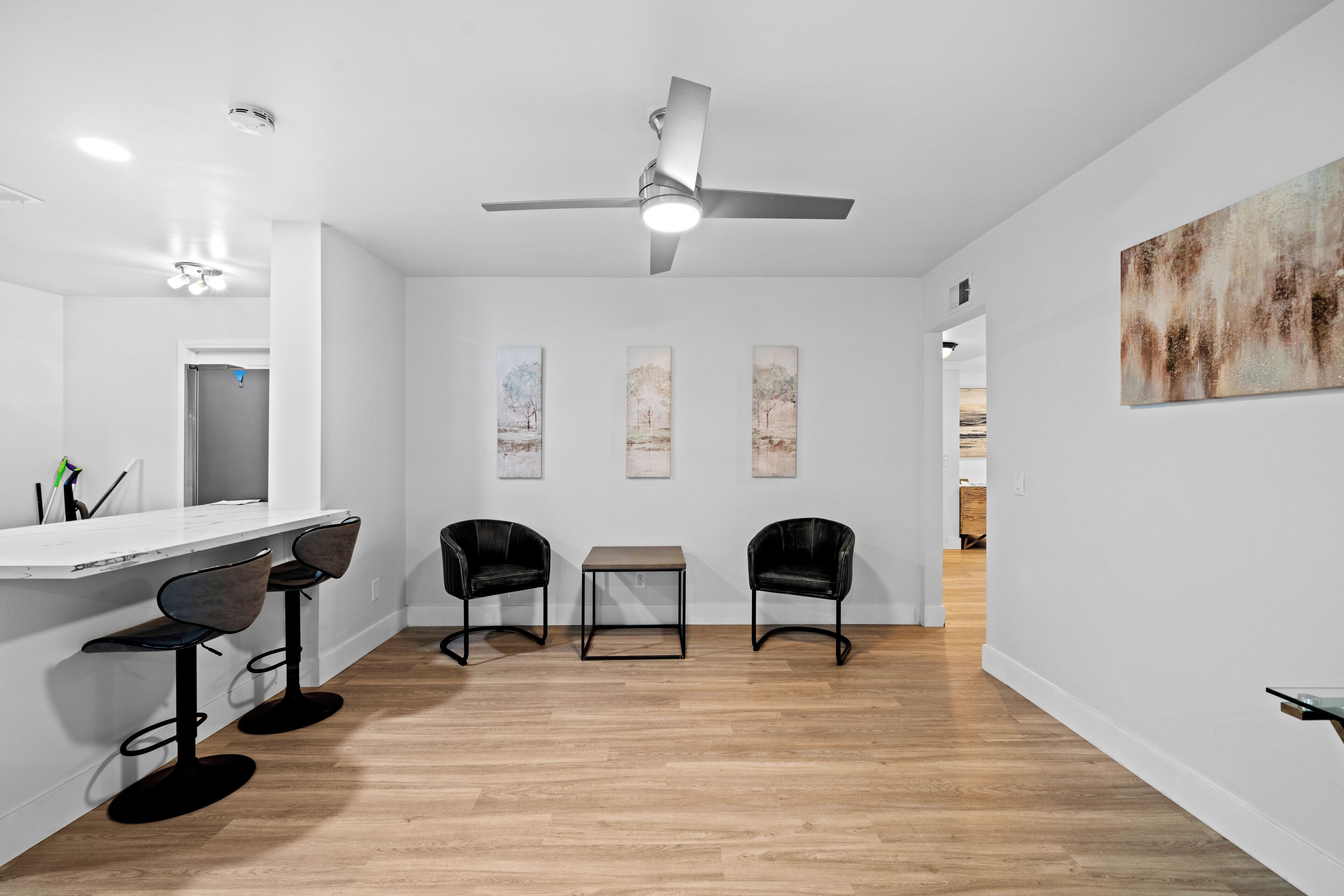 Une cuisine moderne avec un plan de travail blanc, des tabourets de bar noirs, une table centrale et un ventilateur de plafond.