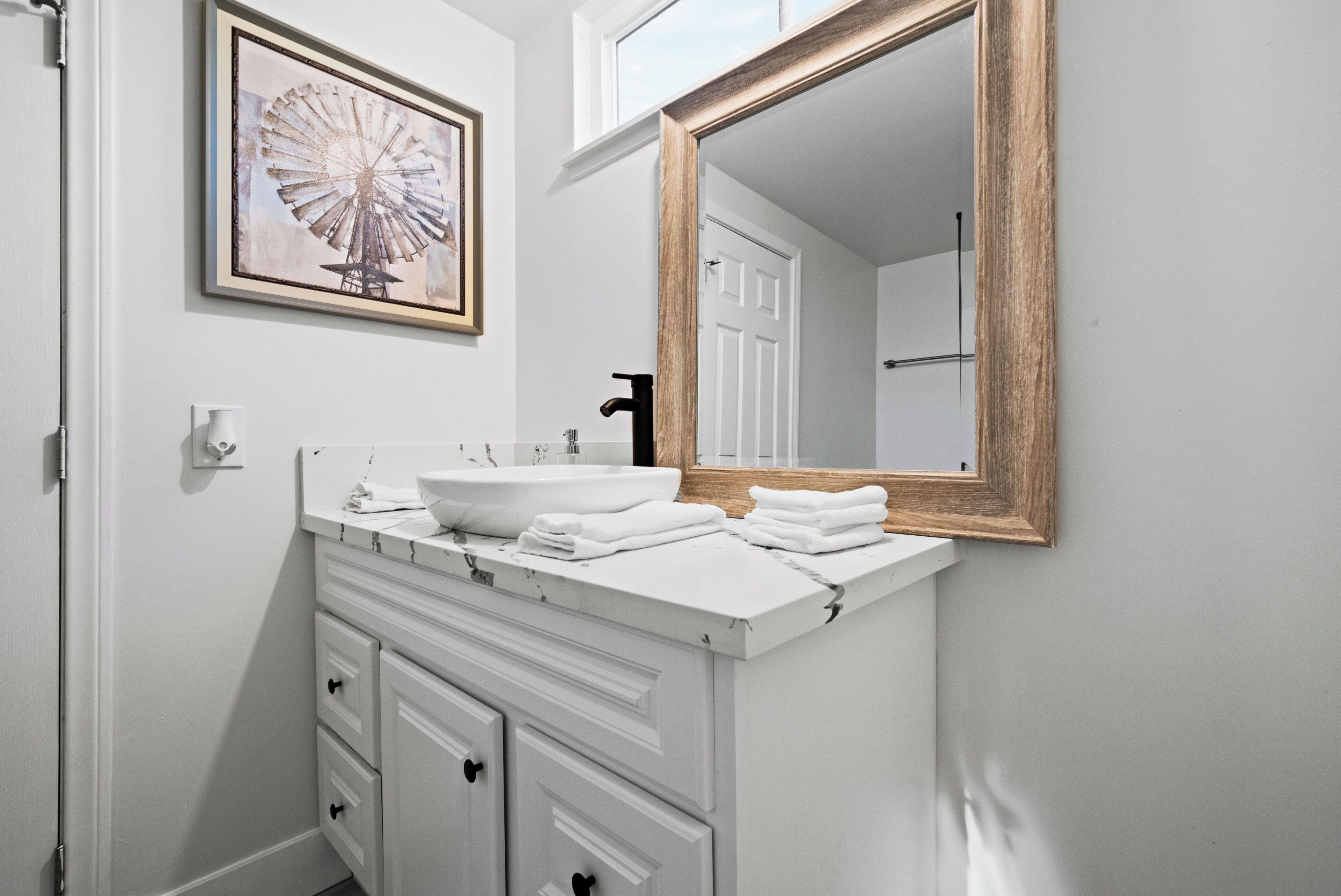 A bathroom with a white sink, a large mirror, and a framed picture on the wall.