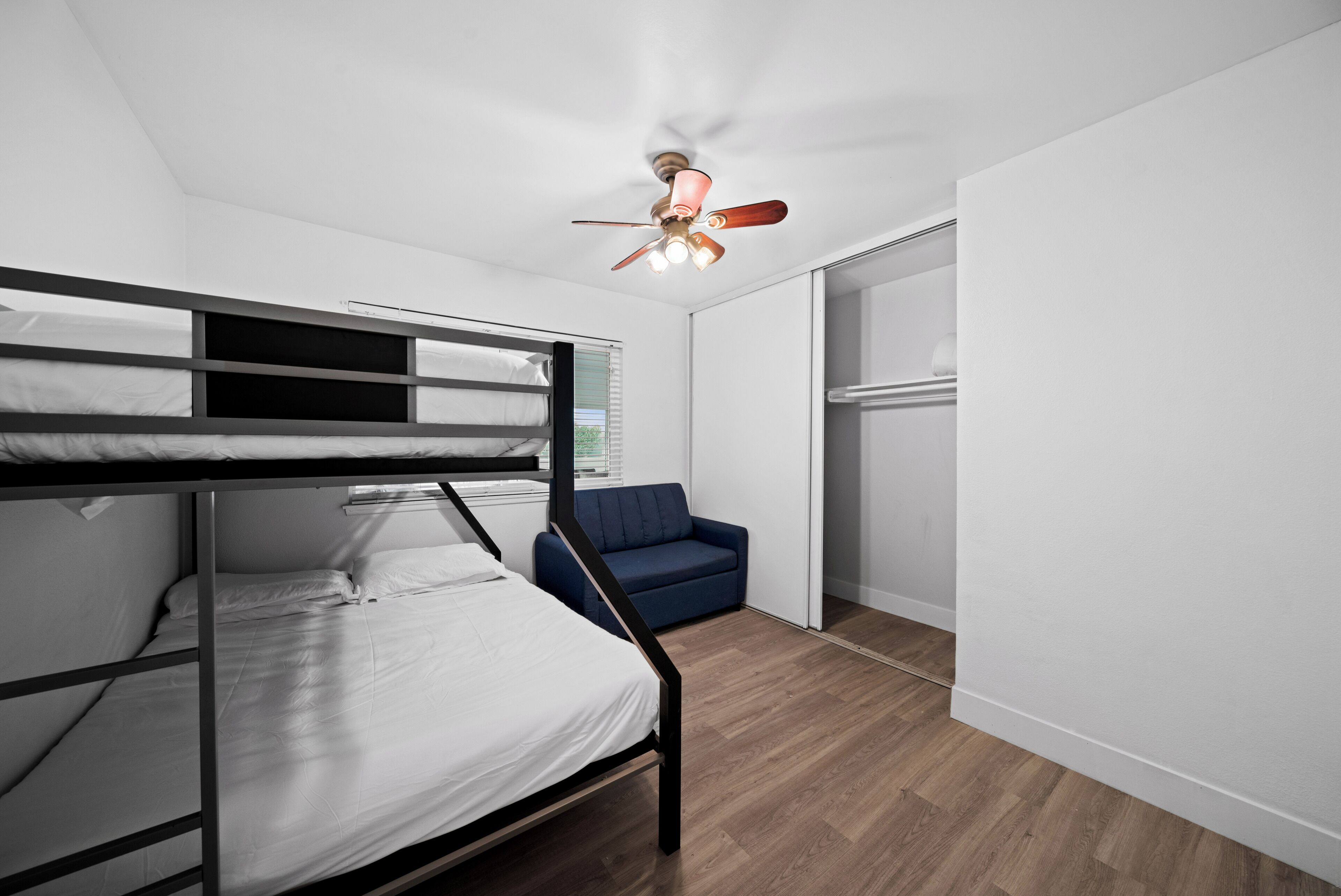 Une chambre avec un lit superposé, un ventilateur de plafond, un canapé bleu et un placard à portes coulissantes.