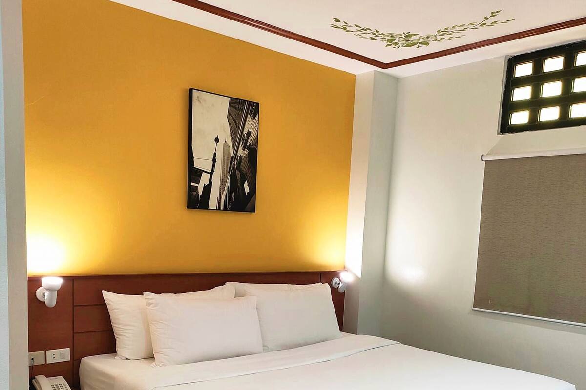 A hotel room with a large bed, wooden headboard, a nightstand with a phone, and a wall-mounted picture.