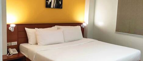 Habitación de hotel con una cama grande, cabecera de madera, una mesita de noche con teléfono y un cuadro colgado en la pared.