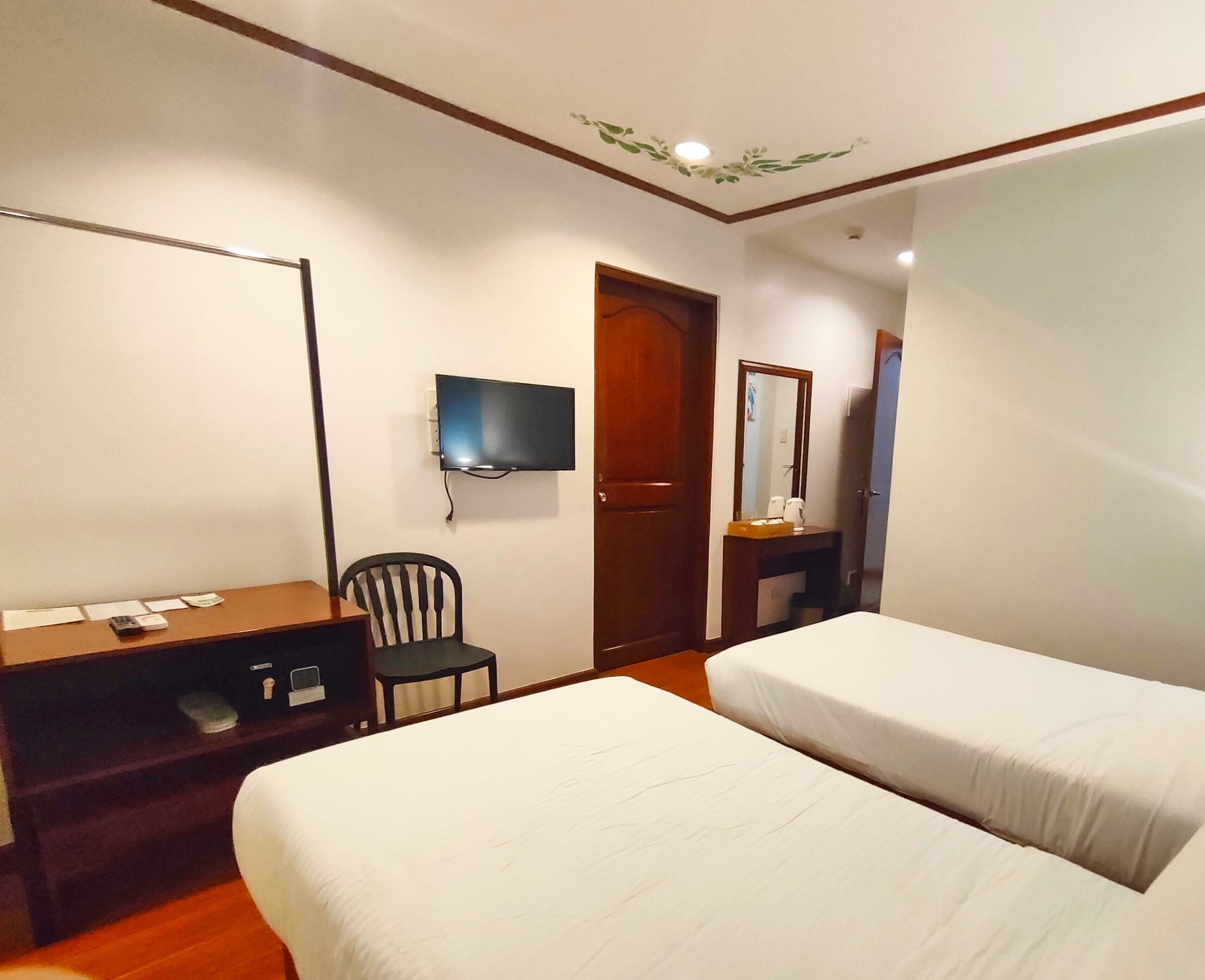 A hotel room with two single beds, a desk with a chair, a television mounted on the wall, and a door leading to a bathroom.