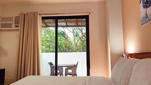 Quarto de hotel com cama, mesa e cadeiras, janela com cortinas e ar-condicionado fixado na parede.