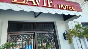 Exterior do LAVIE HOTEL com uma placa vermelha e dourada chamativa, cornija decorativa e janelas com grades.