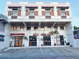 A multi-story building with a white facade and red accents. It features several commercial establishments including a hotel, a nail salon, and a salon.