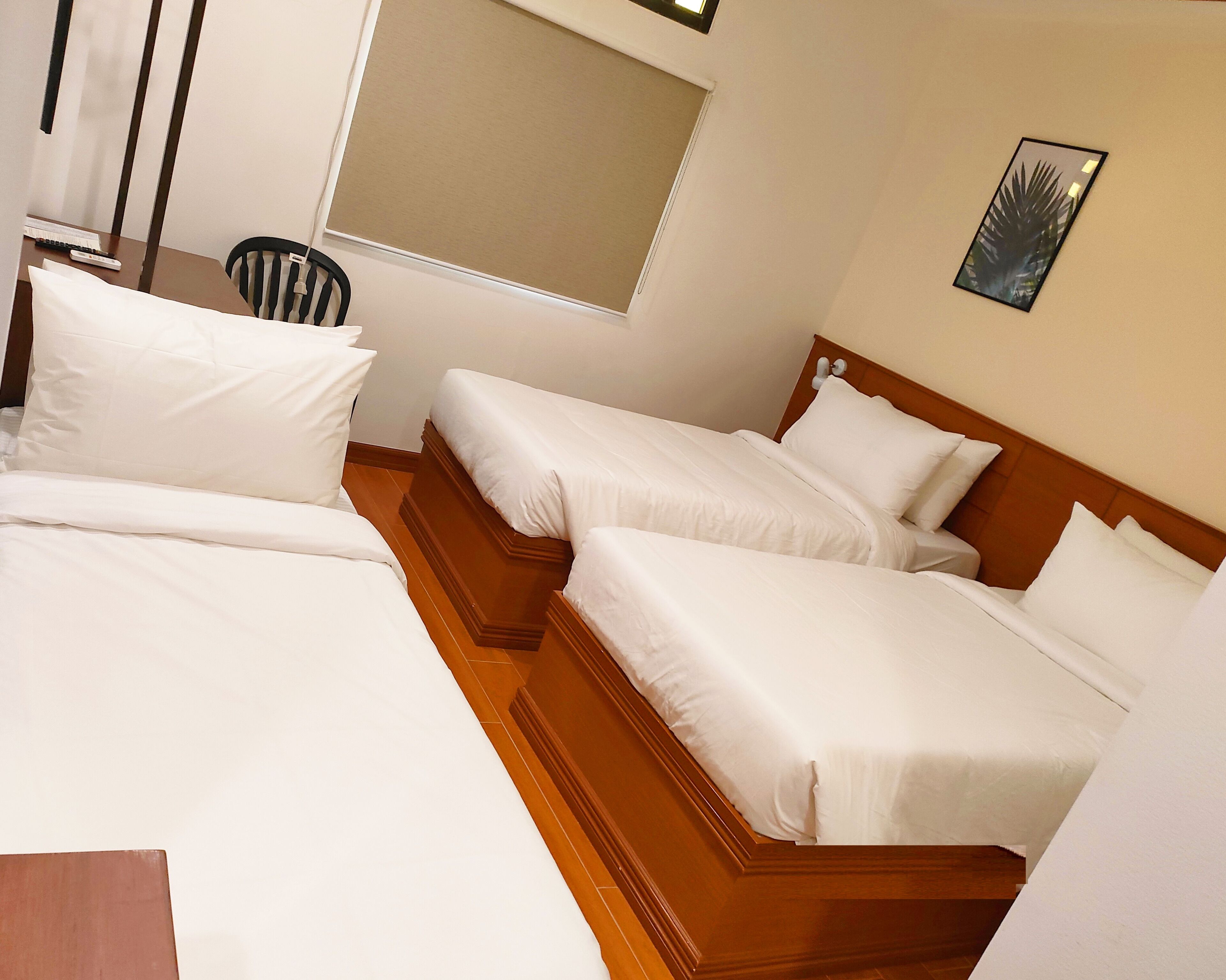 Una habitación de hotel con tres camas individuales, un cabecero de madera, una ventana y una silla.