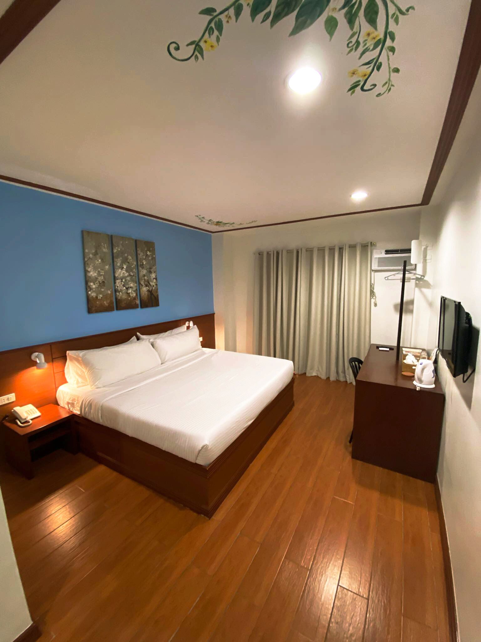 A hotel room with a large bed, a desk, a chair, a telephone, and a television.