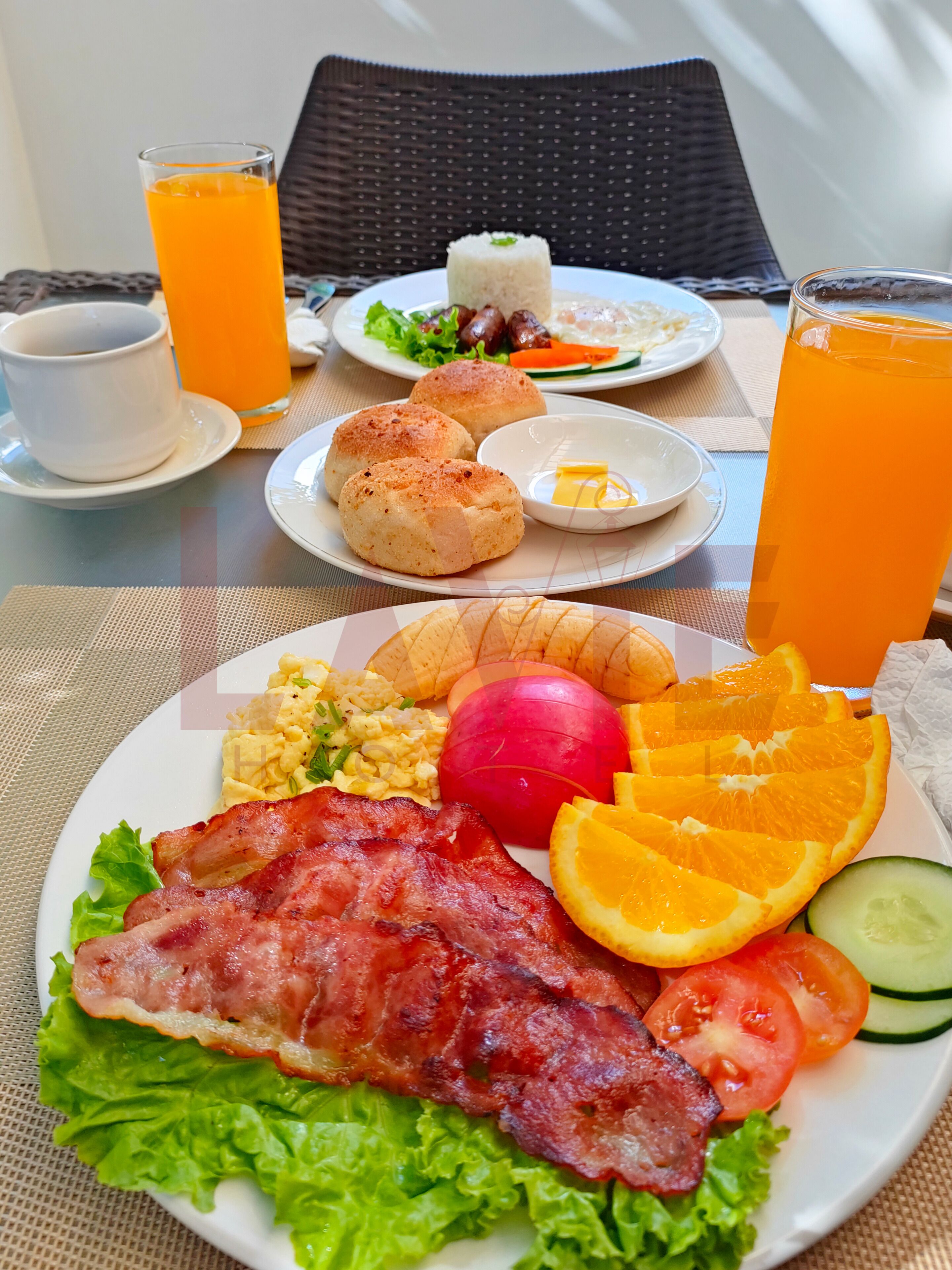 A breakfast setting with plates of food, including bacon, eggs, toast, and fruit, along with glasses of orange juice.