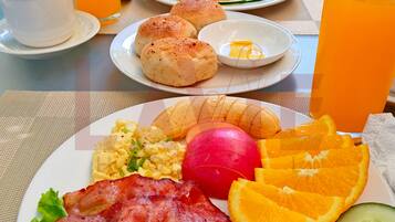 A breakfast setting with plates of food, including bacon, eggs, toast, and fruit, along with glasses of orange juice.