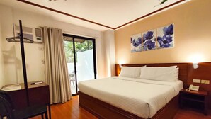 Quarto de hotel com uma cama grande, uma escrivaninha com cadeira, telefone e um quadro de flores na parede.