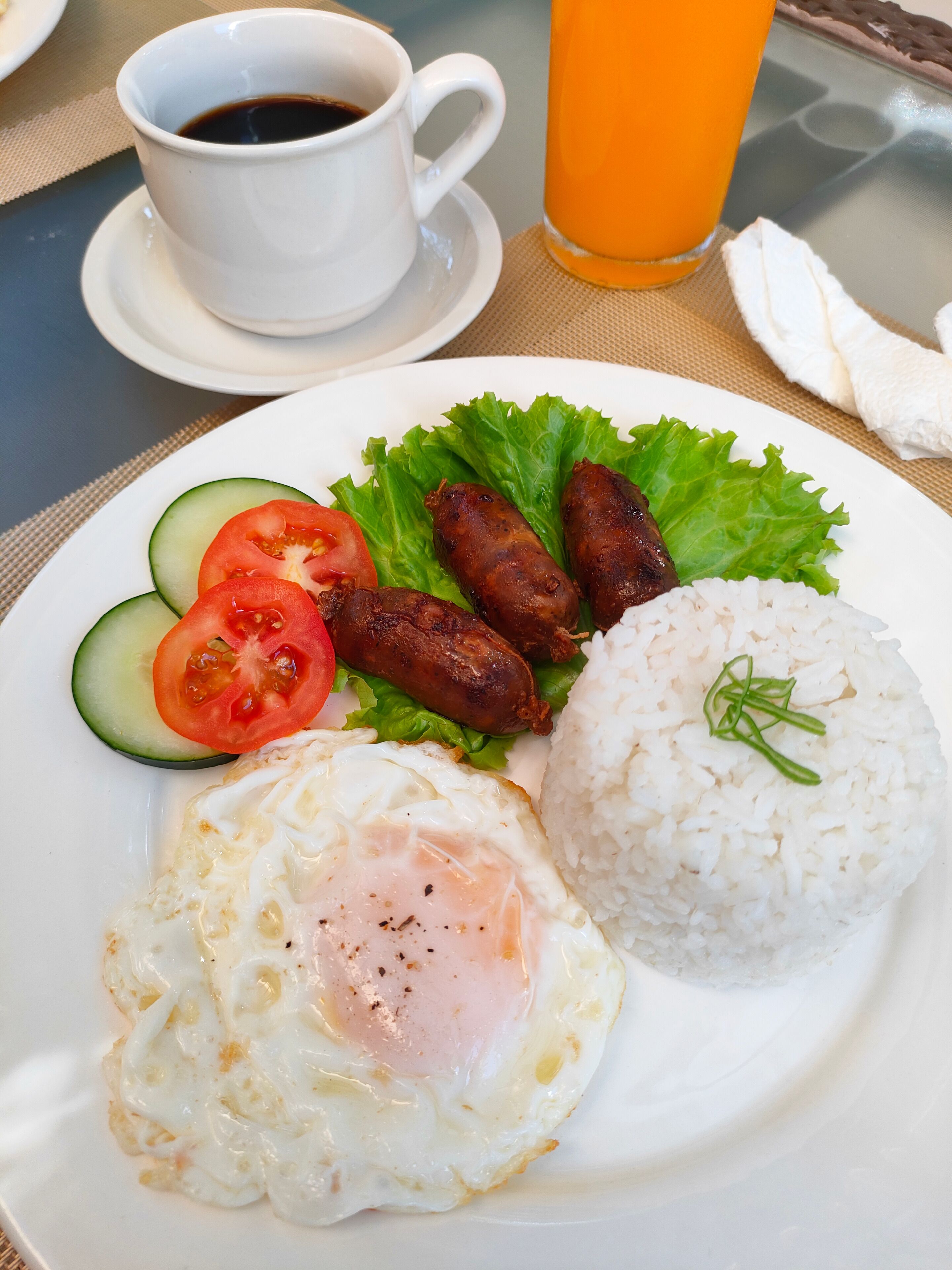 Un plato con huevo frito, arroz, salchichas y verduras.