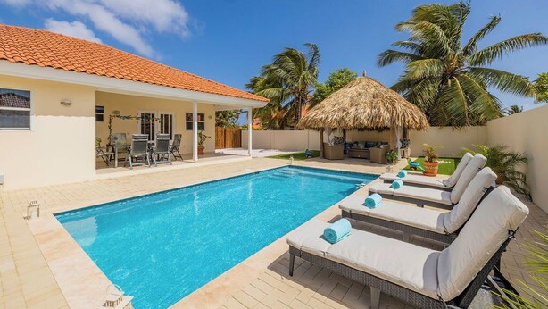 Une piscine avec des chaises longues, un patio couvert et une structure à toit de chaume.